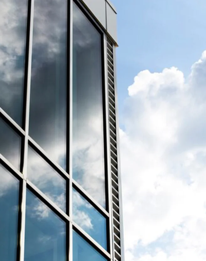 Fachada de vidrio y perfilería metálica en edificio moderno con reflejo del cielo